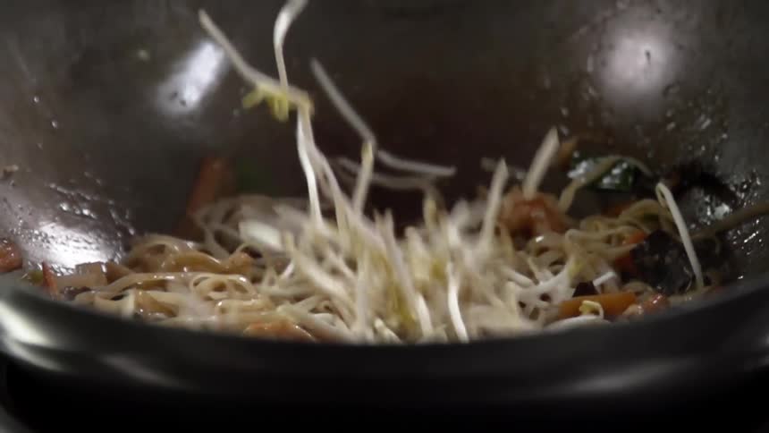 Bean sprouts are added to noodles and vegetables in wok