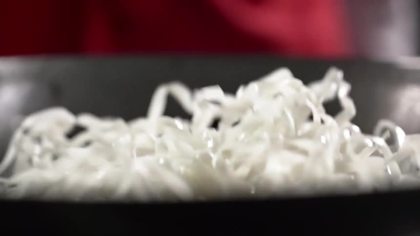 Person wearing red drops noodles into wok