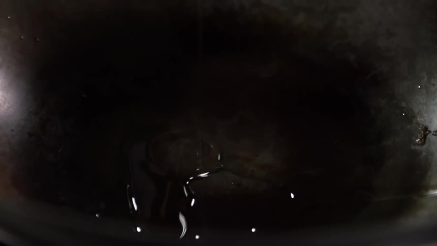 Vegetable oil pouring on the blackened surface of a wok