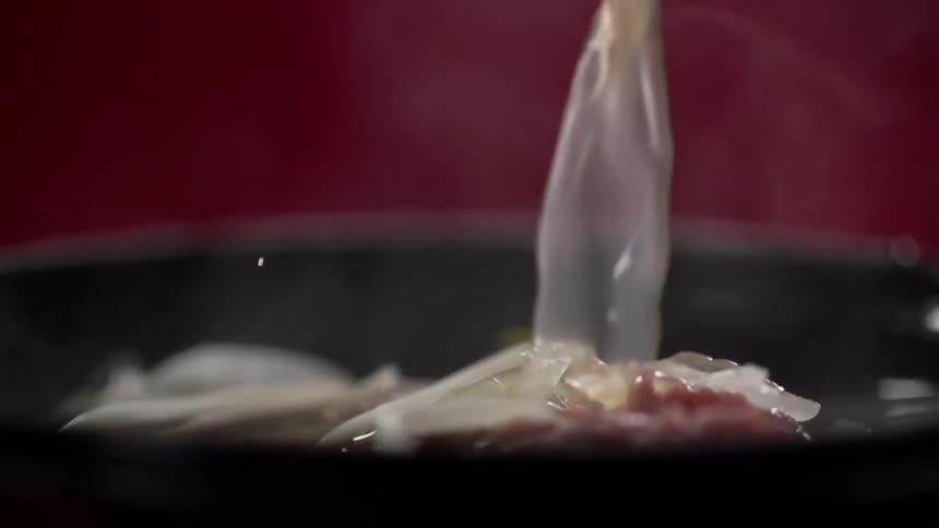 Clear yellow broth pouring over noodles inside a black bowl