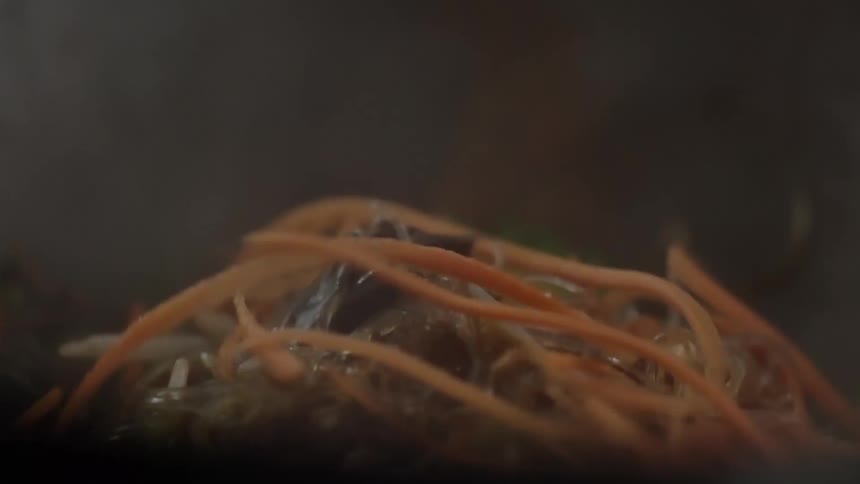 Sliced carrots being dropped into a steaming skillet of food