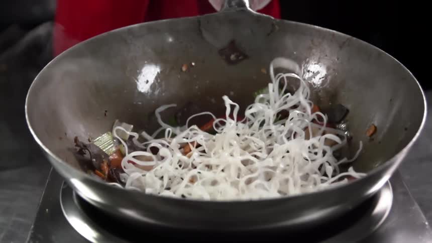 White rice noodles are added to a wok with shrimp and vegetables