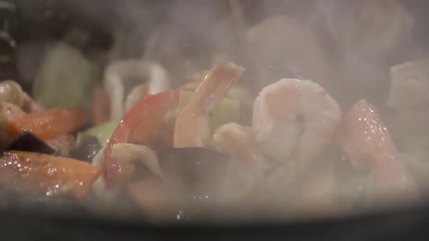 Seafood and vegetables are tossed in a stir fry pan with chopsticks