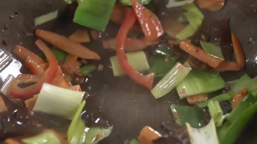 Chopsticks mixing assorted vegetables frying inside a steaming hot wok
