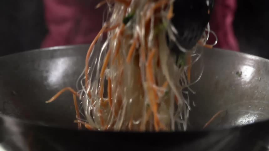 Glass noodles tossed on a steaming hot wok using chopsticks and draining spoon