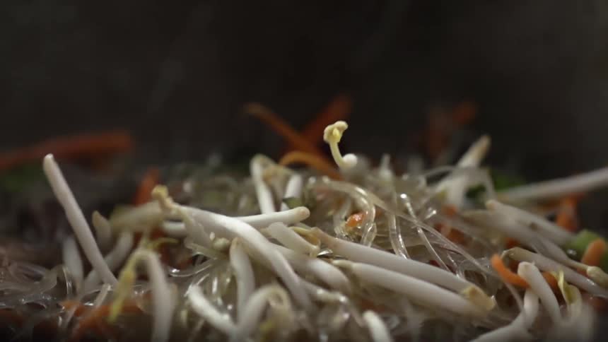 Bean sprouts fall onto cellophane noodles in steaming pan