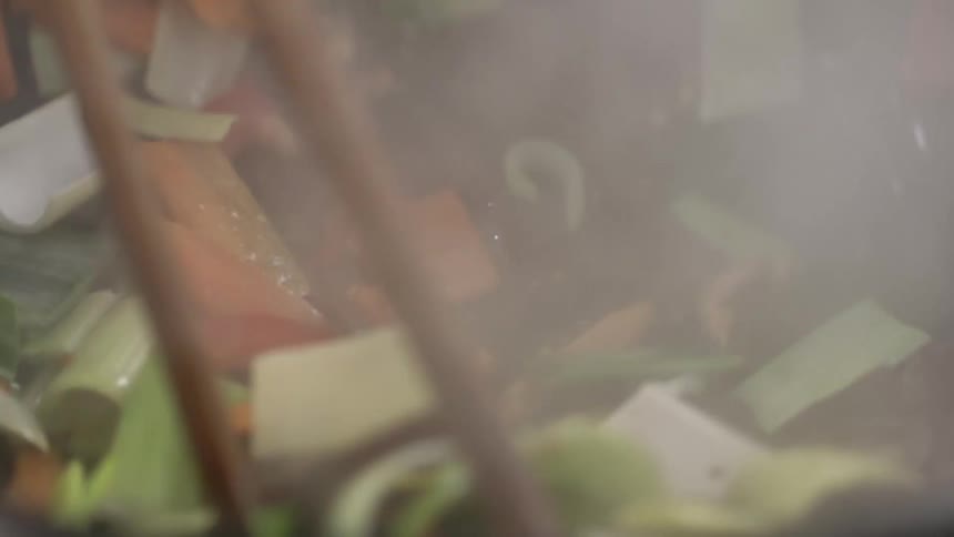 Close up of tongs sauteing vegetables in stir fry