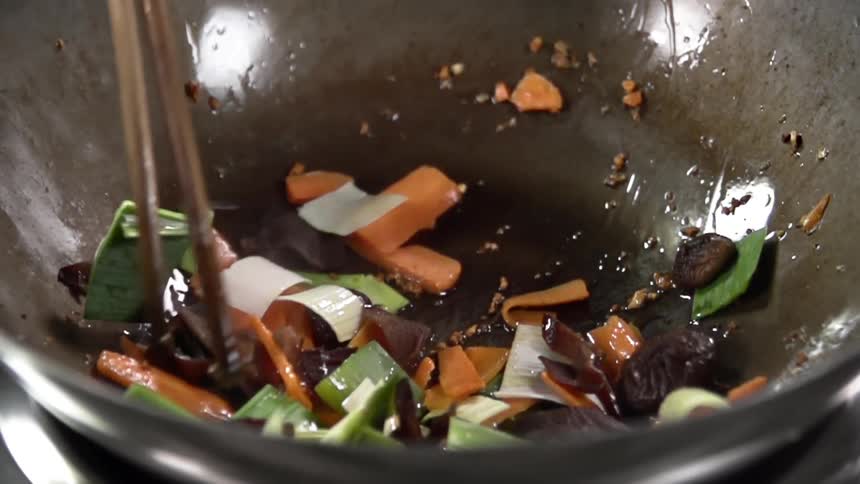 A person uses chopsticks to stir vegetables in a wok