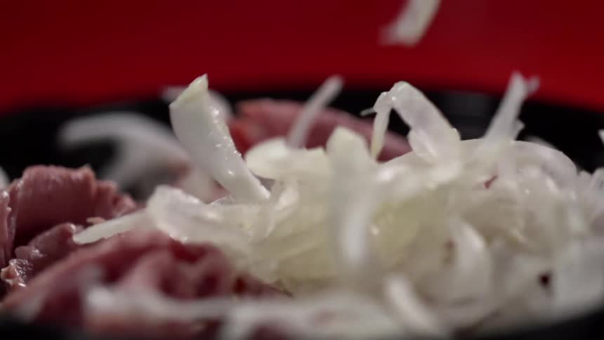 White onion shreds are added to meat in black bowl against red background