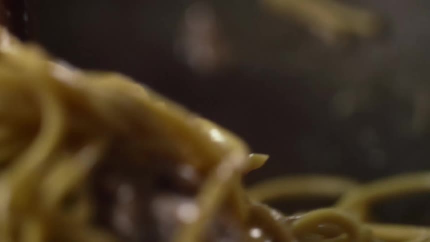 Chow mein noodles and beef are stirred with chopsticks in a wok