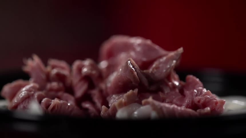Meat falling into a black bowl with a red background