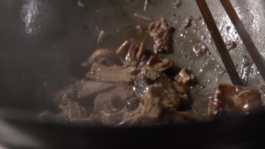 Meat is cooked and stirred with chopsticks in a wok