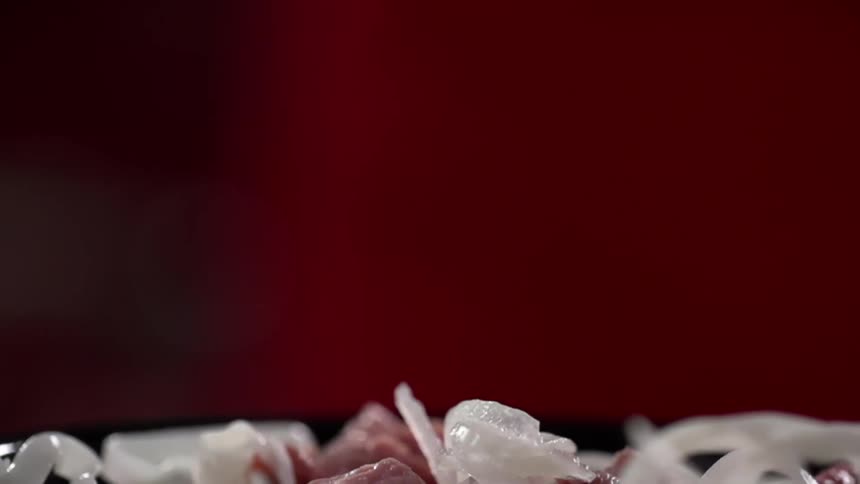 Sliced onions falling onto a plate of raw meat