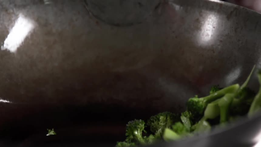 Broccoli added to glistening wok reflecting lights