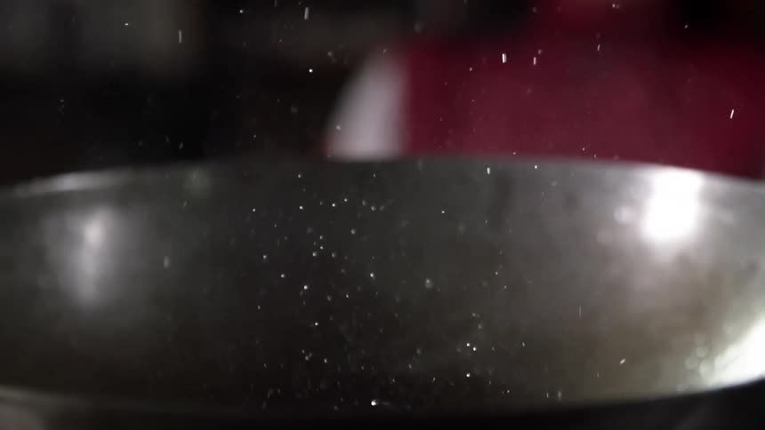 Specks of cooking oil fly up from a hot wok