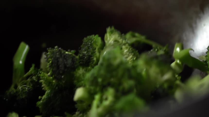 Broccoli florets drop into metal bowl reflecting light