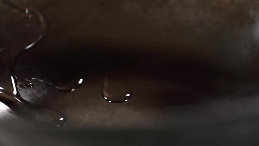 A clear and viscous liquid is slowly drizzled onto a dark metal surface