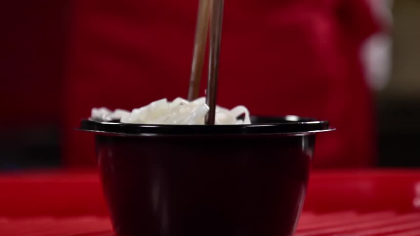 Noodles being placed in a bowl with chopsticks