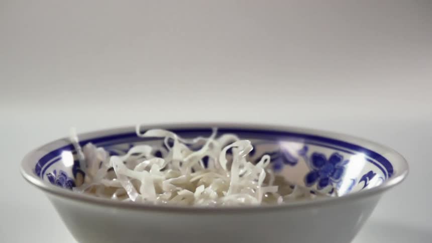 A pile of white noodles is dropped into a glass bowl with a blue floral pattern