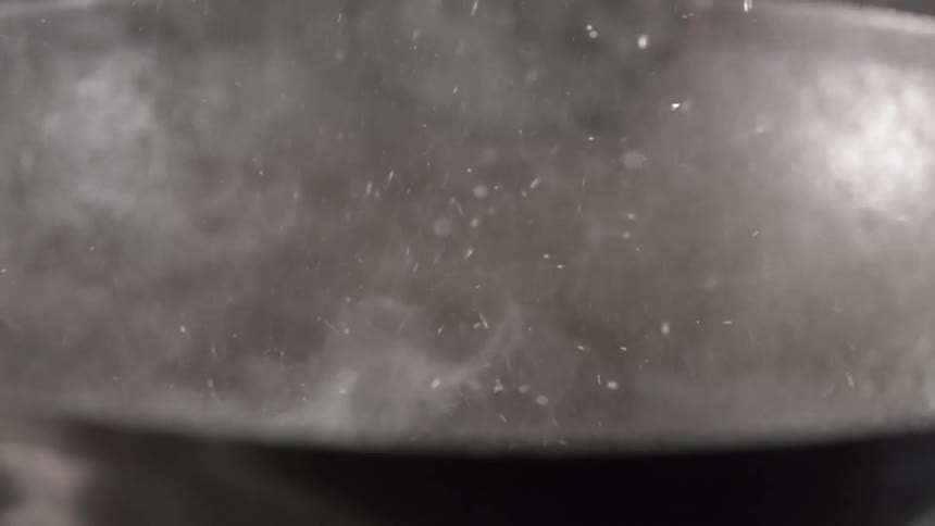 A wok with smoke with oil cooking and splashing up