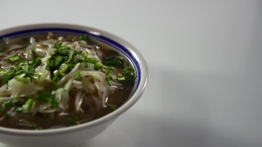 Chives falling on top of a bowl of soup placed for a photo shoot