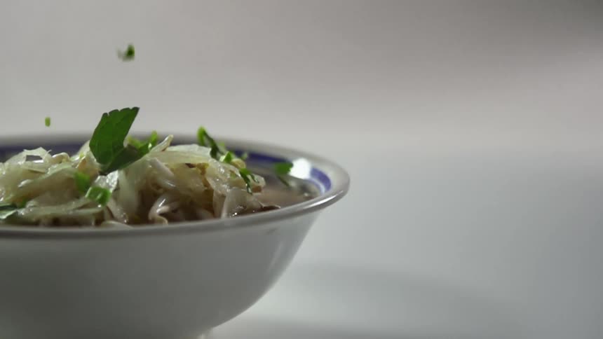 Green leafs falling over the vegetables floating in soup inside a ceramic bowl
