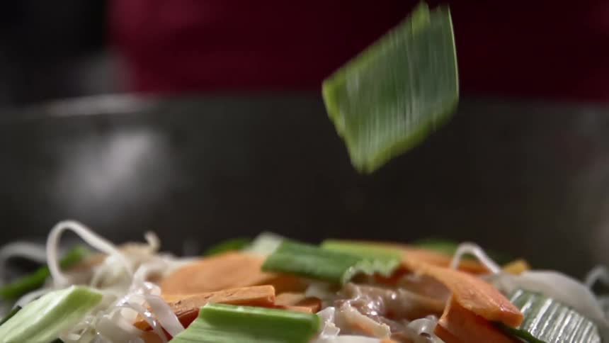 Vegetables are added to noodles and meat in wok