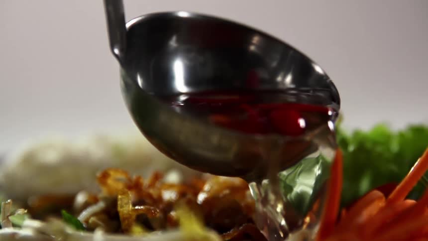 A spoon with sauce being poured onto vegetables