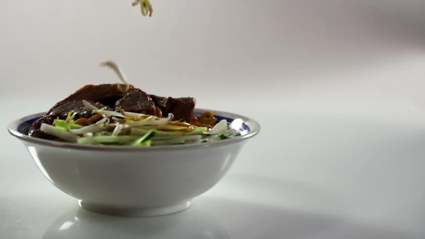 Bean sprouts fall into a bowl of beef noodles and vegetables