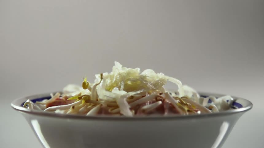 A bowl of vegetables with onions falling onto it with a gray background