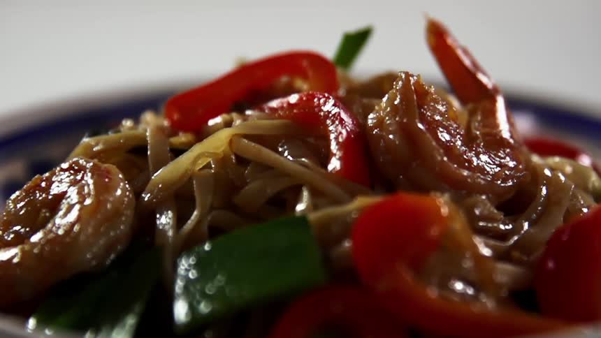 Stir fried noodles with shrimp and bell peppers are plated on a blue plate