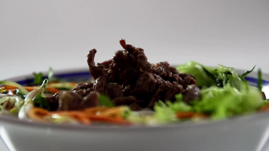 Beef being poured into a bowl with vegetables