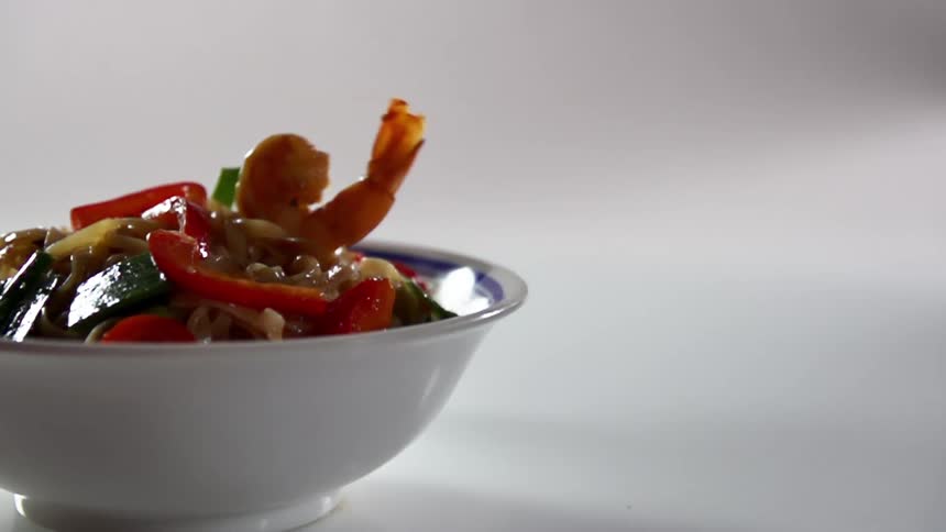 Shrimp dropping into a bowl of stir fry