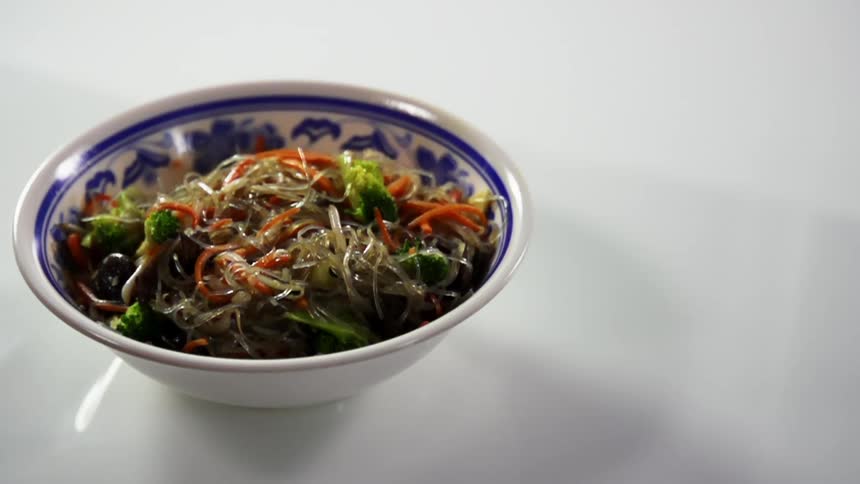 A bowl with food with broccoli falling into the bowl