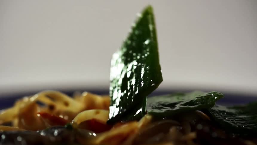 Lo mein with vegetables with a leafy vegetable falling onto it