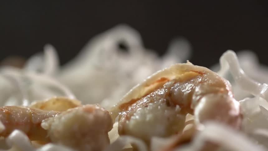 Several pieces of cook shrimp are dropped on top of a bed of rice noodles