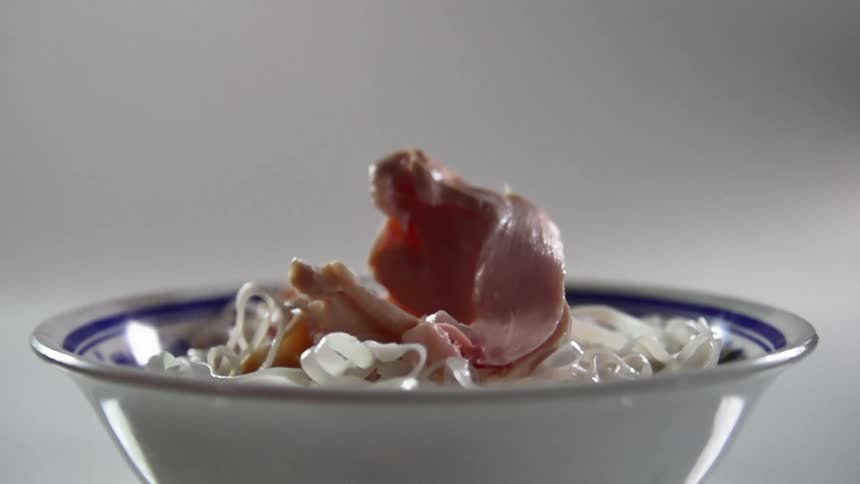 Slices of raw chicken are dropped into a bowl filled with rice noodles