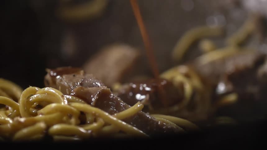Sauce being poured on meat and noodles