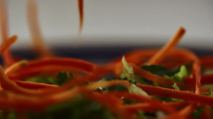 Strips of sliced carrots falling onto a plate of green leafy vegetables