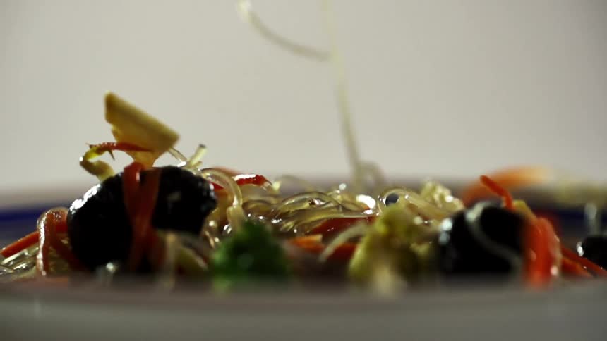 Glass noodles with vegetables drops into a ceramic dish