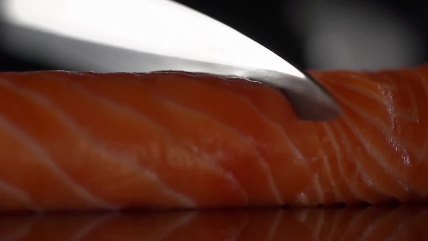 Close up of a cook cutting salmon with a sharp knife in studio