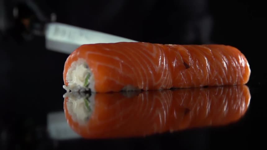 Cook with black gloves cuts sushi in half in studio