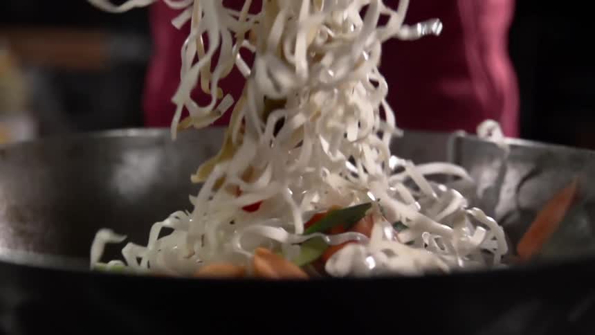 A person stirs noodles and vegetables in a pan