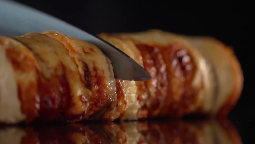 A knife cuts through a log of meat