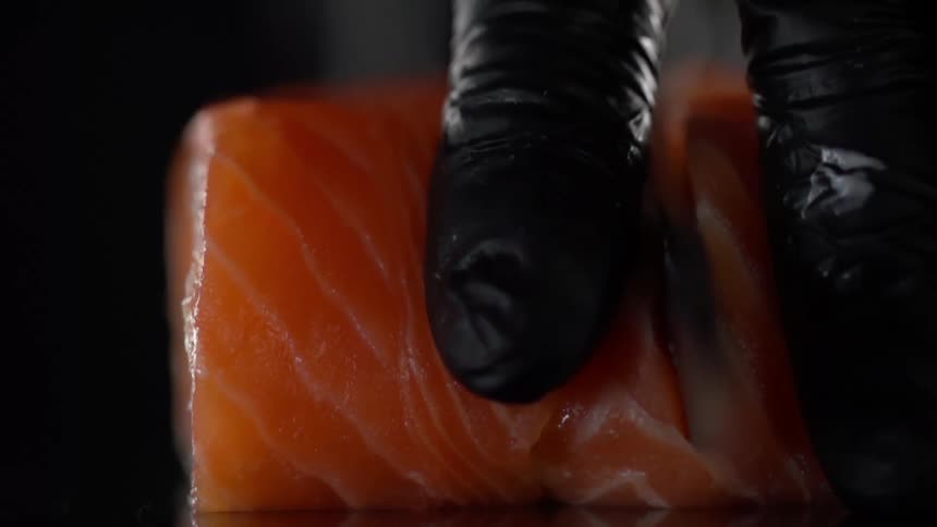 Man with black gloves cuts salmon in half for sushi with a knife