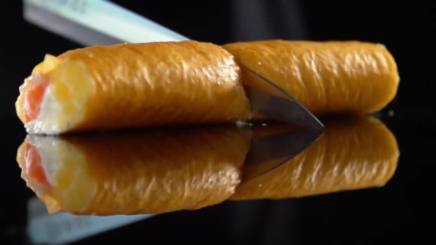 Knife cuts stuffed roll sitting on black reflective surface in half