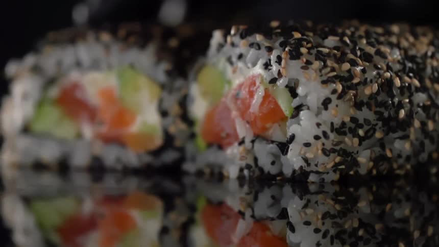 Sushi rolls being arranged side by side on a reflective counter