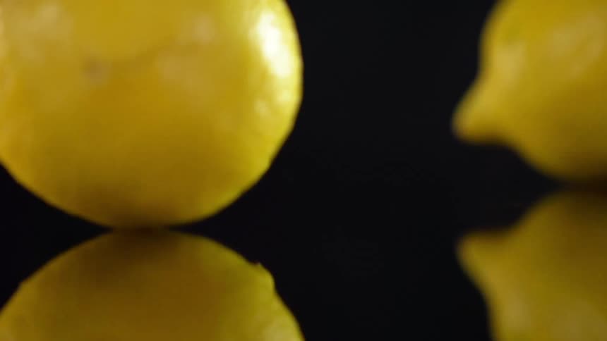 A trio of lemons drop onto a dark reflective surface where they bounce and gently roll around