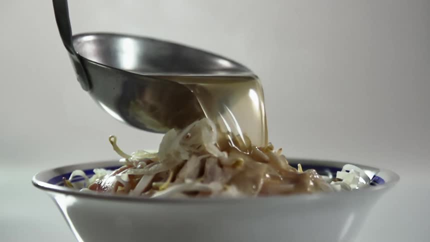 Soup pours from a metal ladle onto a bowl of food