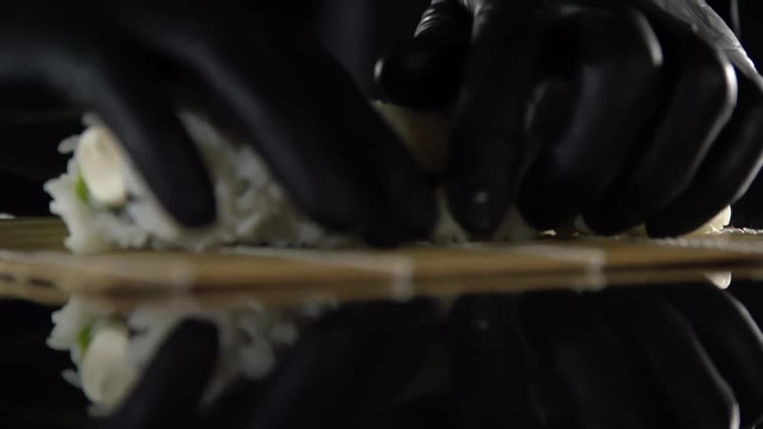 Chef wearing black latex gloves wraps a sushi roll over a bamboo mat